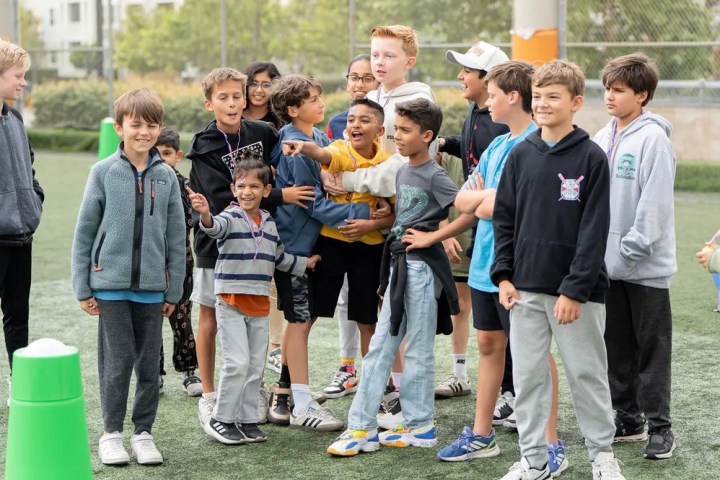 Group of children smiling and pointing on a grass field.