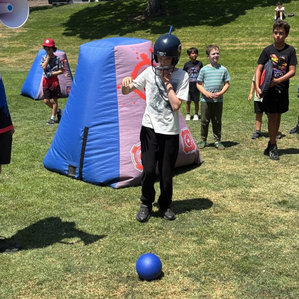 Kids playing with inflatable bunkers and balls on a grassy field.