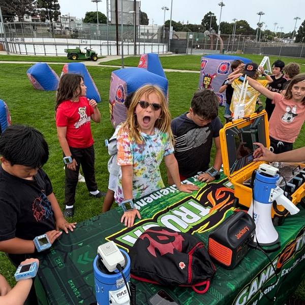 Children at a park gathering near a table with equipment and colorful inflatable bunkers.