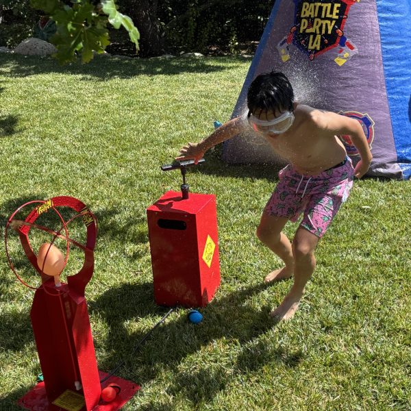 Child playing with a water game outdoors, splashing water while running in a grassy area.
